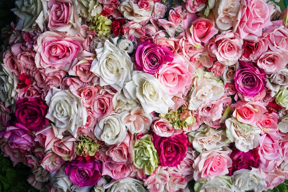 A densely arranged floral composition featuring a variety of roses in shades of pink, white, and purple, complemented by clusters of pale green carnations. The flowers are arranged in a lush, full bou